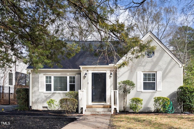 new england style home featuring roof with shingles, brick siding, crawl space, and fence