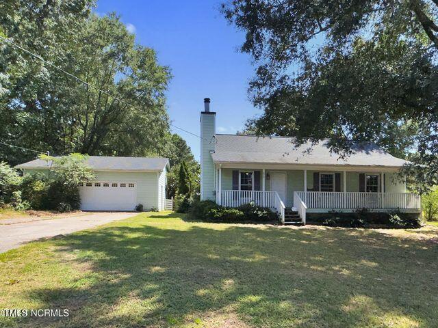 ranch-style home featuring a chimney, an outbuilding, covered porch, and a front yard