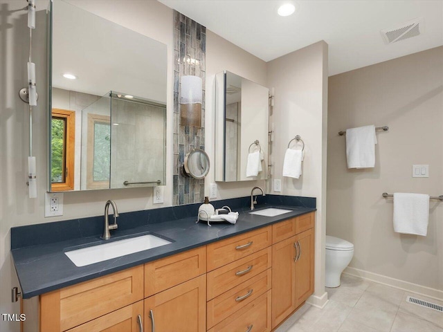 full bath featuring a tile shower, baseboards, tile patterned floors, double vanity, and toilet