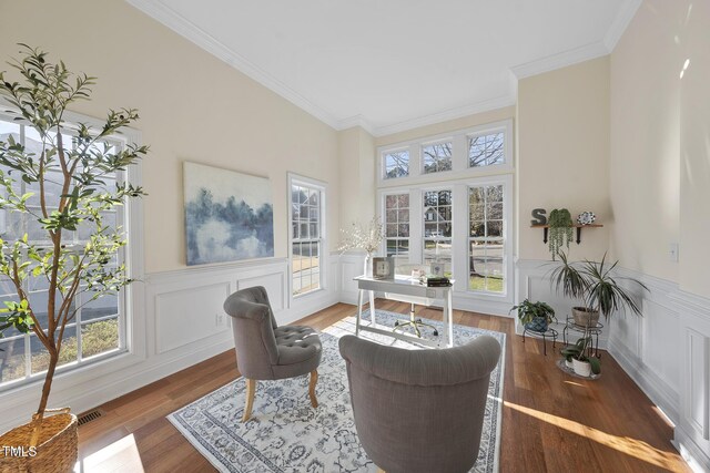 living area with visible vents, wood finished floors, a wealth of natural light, and crown molding