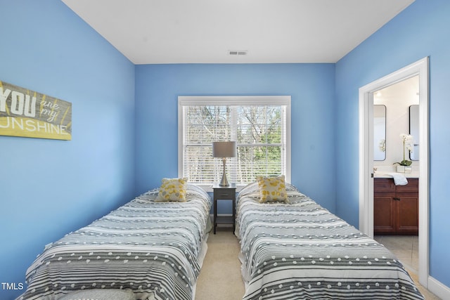 bedroom with light colored carpet, visible vents, and ensuite bath