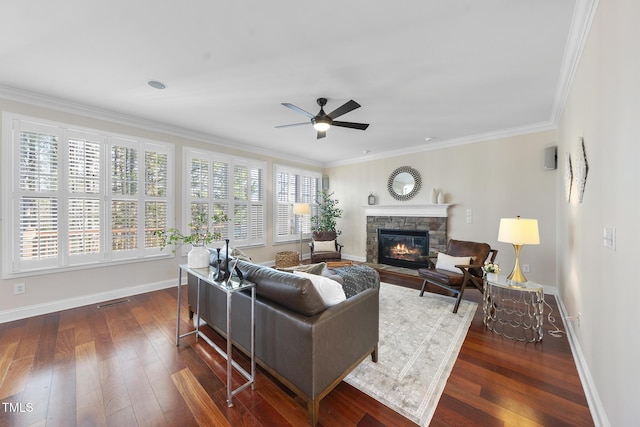 living area with baseboards, dark wood finished floors, ceiling fan, ornamental molding, and a stone fireplace