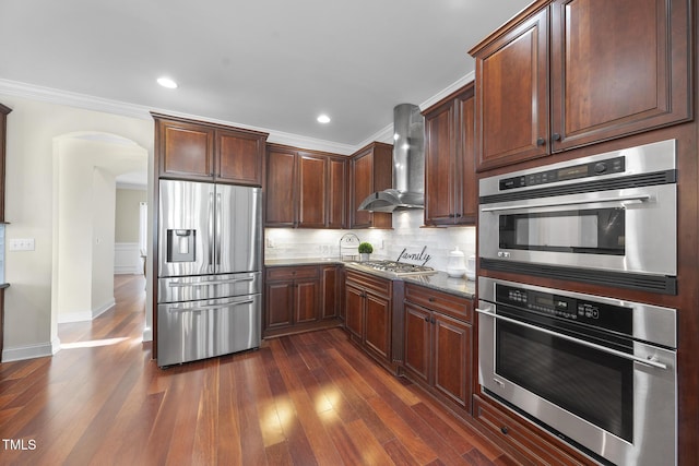 kitchen with arched walkways, stainless steel appliances, dark wood-type flooring, wall chimney exhaust hood, and tasteful backsplash