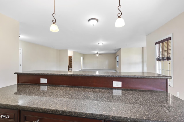 kitchen with dark stone counters, open floor plan, and hanging light fixtures