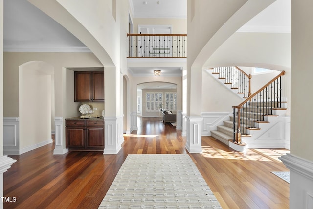 entrance foyer with crown molding, a high ceiling, a decorative wall, and wood finished floors