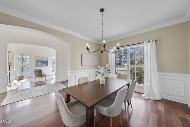 dining area with dark wood-type flooring, a wealth of natural light, wainscoting, and arched walkways