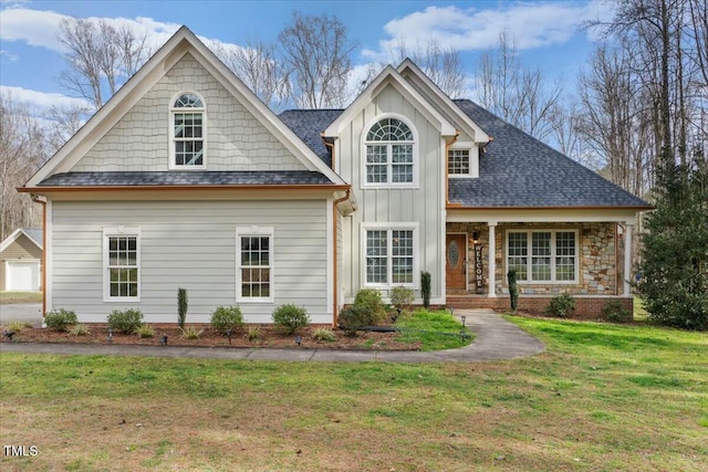 view of front of house with a shingled roof, stone siding, a porch, board and batten siding, and a front yard