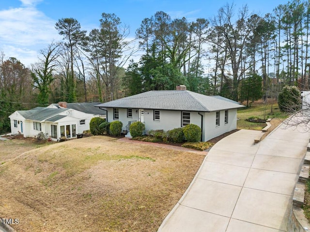 ranch-style home featuring a front yard, concrete driveway, roof with shingles, and a chimney