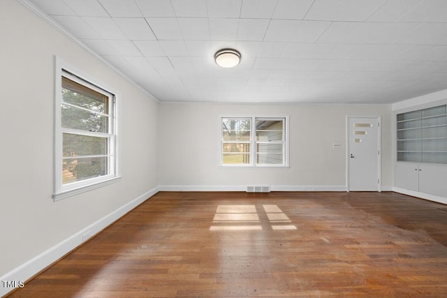 empty room featuring built in shelves, a wealth of natural light, baseboards, and wood finished floors