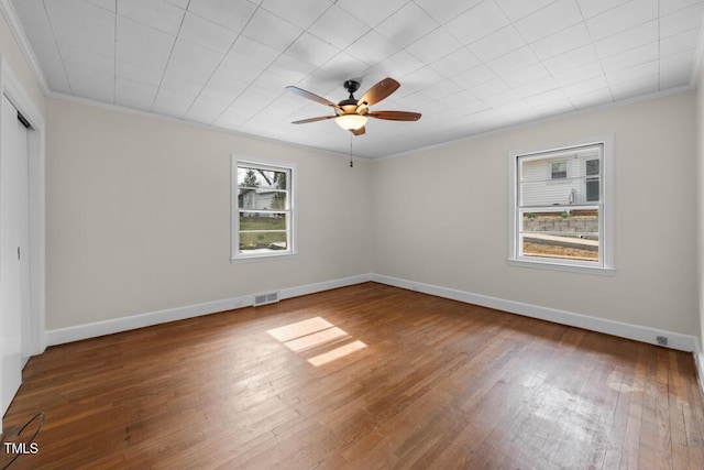 empty room with crown molding, visible vents, ceiling fan, baseboards, and hardwood / wood-style flooring