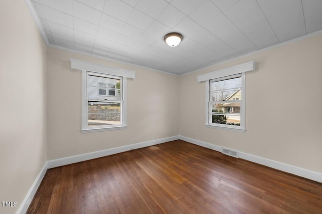 empty room with wood-type flooring, visible vents, crown molding, and baseboards