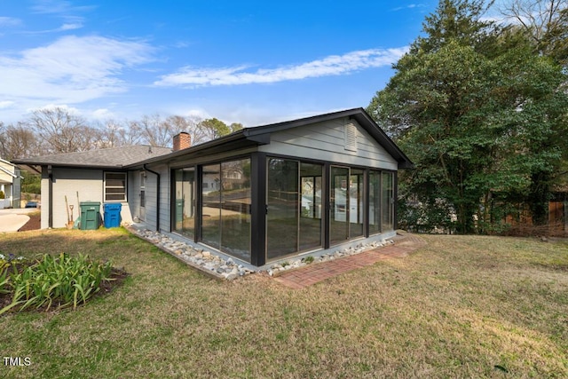 back of property with a sunroom, a lawn, and a chimney