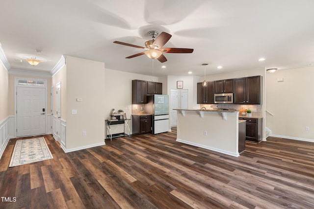 kitchen with dark brown cabinetry, stainless steel microwave, a breakfast bar, and freestanding refrigerator