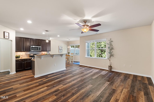 kitchen featuring dark brown cabinetry, a kitchen breakfast bar, backsplash, dark wood-style floors, and stainless steel microwave