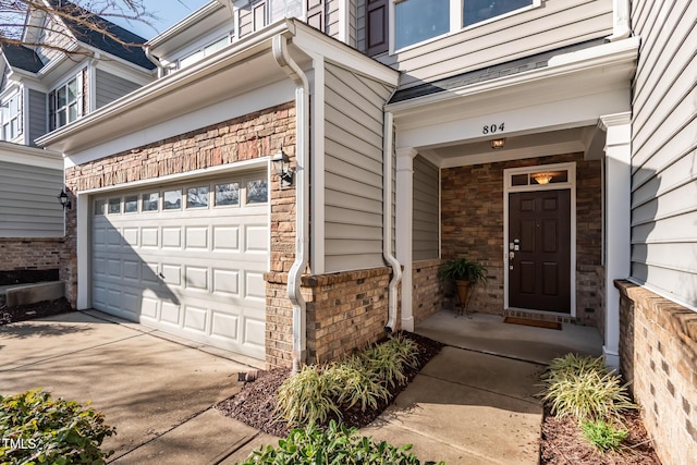 property entrance with a garage, concrete driveway, and brick siding