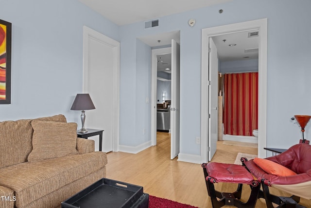 living room with light wood-style flooring, visible vents, and baseboards