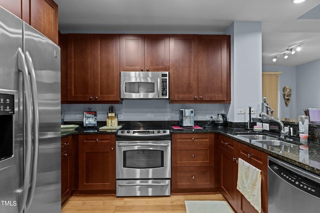 kitchen featuring light wood finished floors, dark stone countertops, appliances with stainless steel finishes, and a sink