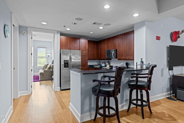 kitchen with recessed lighting, a peninsula, a breakfast bar, light wood-style floors, and appliances with stainless steel finishes