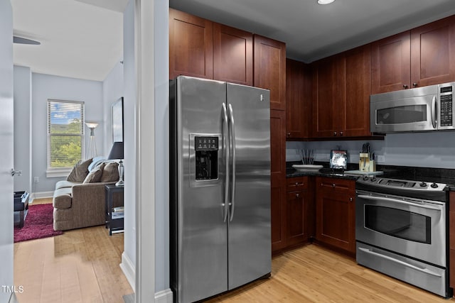 kitchen with light wood finished floors, baseboards, appliances with stainless steel finishes, and open floor plan