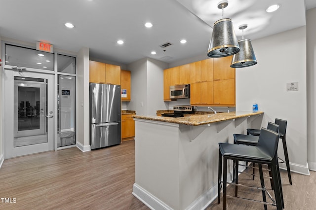 kitchen with light stone counters, a breakfast bar, appliances with stainless steel finishes, light wood-style floors, and a peninsula