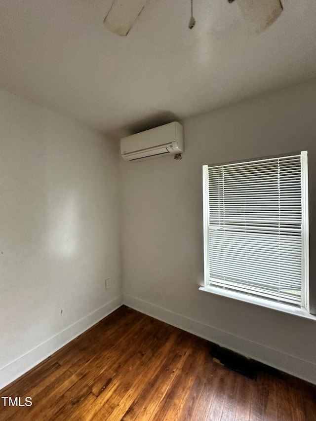 spare room featuring dark wood-style flooring, a wall mounted air conditioner, and baseboards