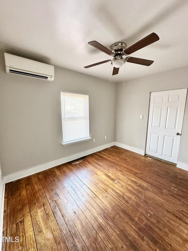 unfurnished room featuring a wall mounted AC, wood-type flooring, and baseboards