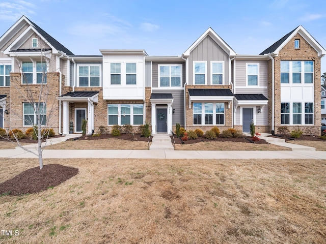 townhome / multi-family property with board and batten siding, a standing seam roof, brick siding, and metal roof