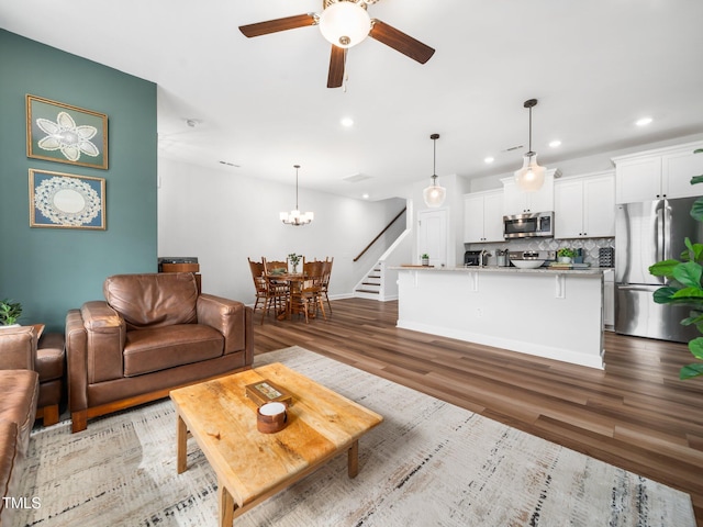 living area with stairs, ceiling fan with notable chandelier, wood finished floors, and recessed lighting