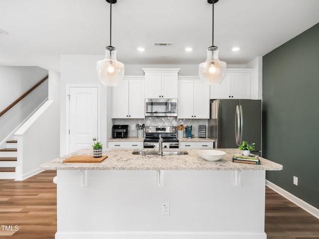 kitchen featuring a breakfast bar, backsplash, appliances with stainless steel finishes, white cabinets, and a sink