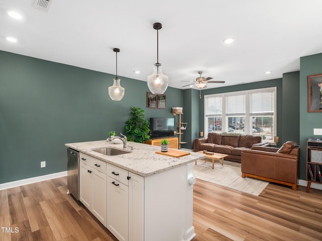 kitchen with hanging light fixtures, light wood-style flooring, stainless steel dishwasher, white cabinets, and a sink