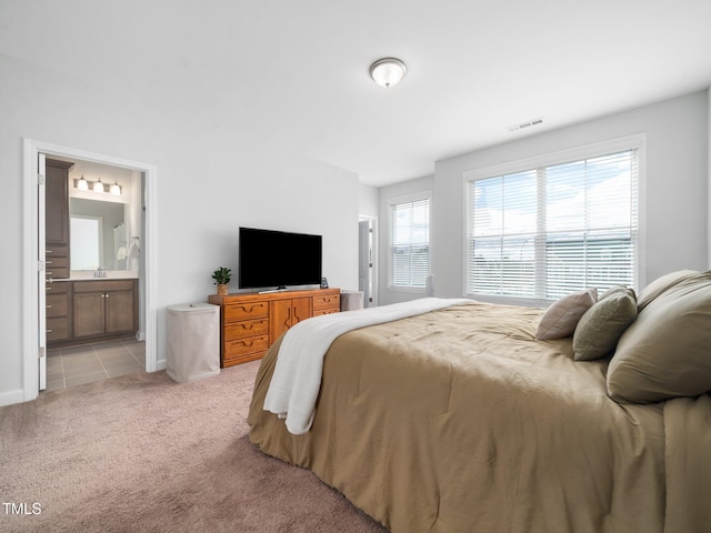 bedroom featuring light colored carpet, visible vents, ensuite bathroom, light tile patterned flooring, and a sink