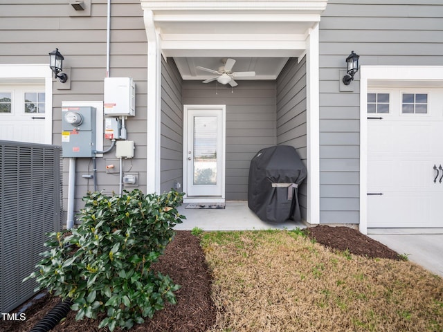 doorway to property with an attached garage, a ceiling fan, and central air condition unit