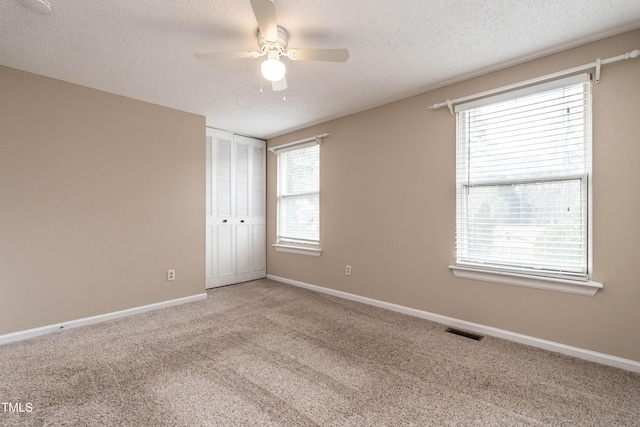 spare room with light colored carpet, visible vents, a ceiling fan, a textured ceiling, and baseboards