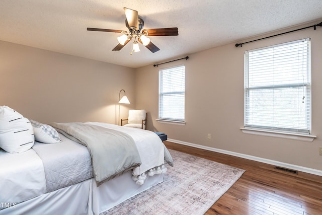 bedroom with a textured ceiling, wood finished floors, visible vents, and baseboards