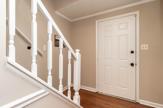 foyer entrance with ornamental molding, a textured ceiling, wood finished floors, baseboards, and stairs