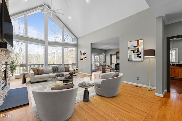 living room featuring visible vents, a stone fireplace, high vaulted ceiling, light wood-type flooring, and baseboards