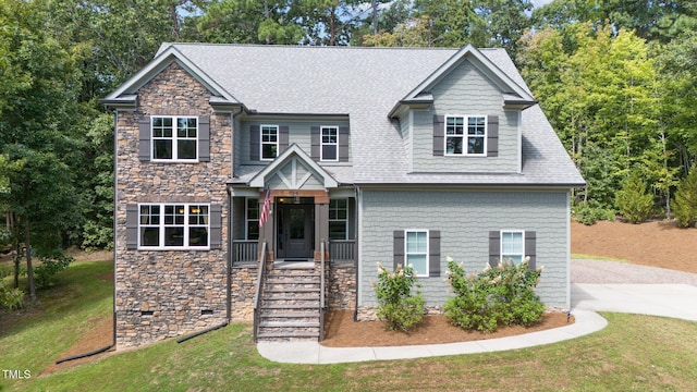 craftsman-style home with stone siding, roof with shingles, and a front yard