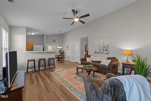 living area with wood finished floors, visible vents, a ceiling fan, vaulted ceiling, and baseboards