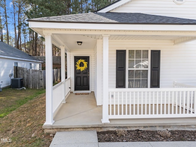 property entrance with central AC unit, a porch, a shingled roof, and fence