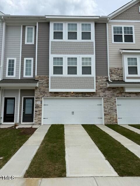 view of property featuring stone siding, concrete driveway, a garage, and a front lawn