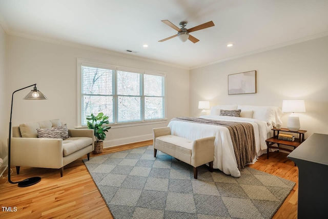 bedroom with light wood finished floors, visible vents, crown molding, and baseboards