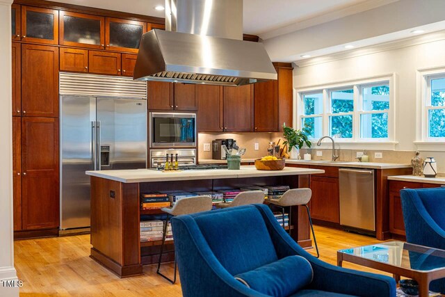 kitchen with light wood-style flooring, crown molding, island range hood, built in appliances, and light countertops