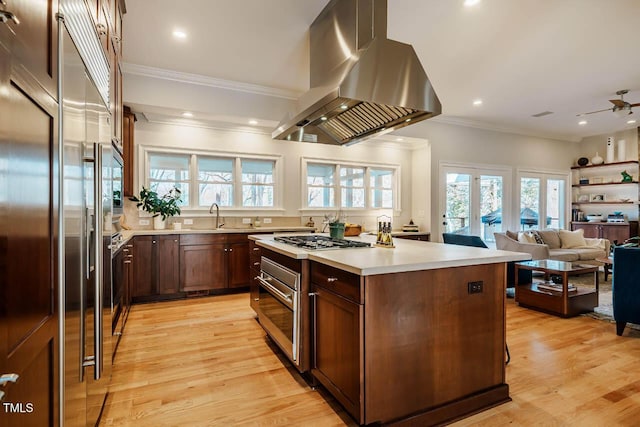 kitchen featuring ornamental molding, island exhaust hood, light wood-style floors, appliances with stainless steel finishes, and light countertops