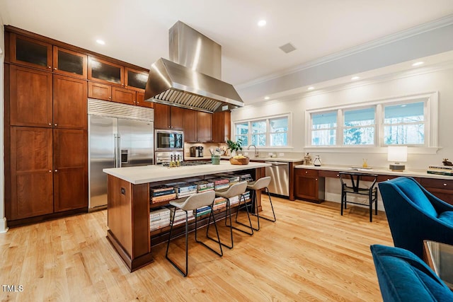 kitchen with built in appliances, light countertops, a kitchen breakfast bar, island exhaust hood, and light wood-style floors