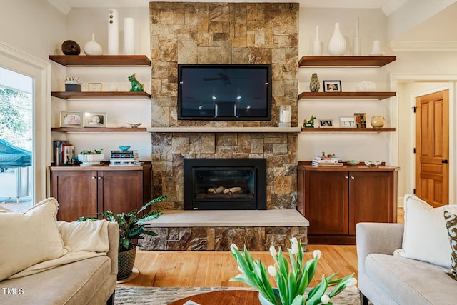 living room with a stone fireplace, crown molding, and wood finished floors