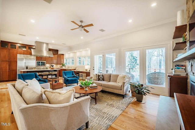 living area with a wealth of natural light, light wood-style floors, and ornamental molding