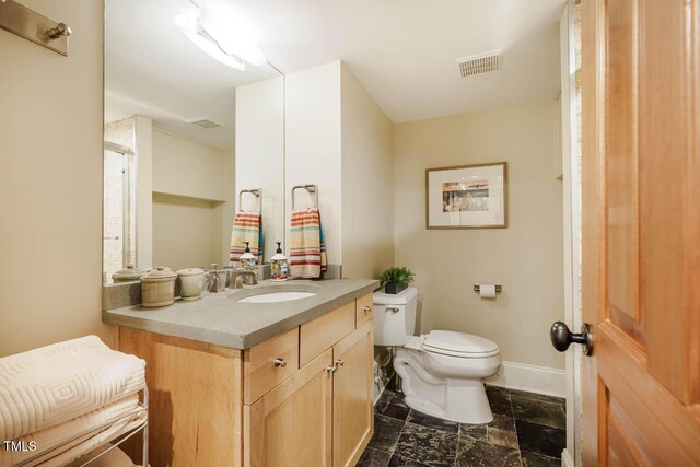 bathroom with visible vents, toilet, stone finish flooring, baseboards, and vanity