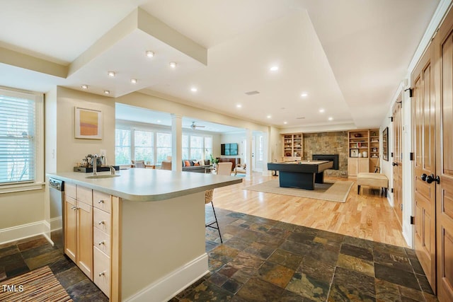 kitchen with baseboards, stone tile flooring, light countertops, stainless steel dishwasher, and open floor plan