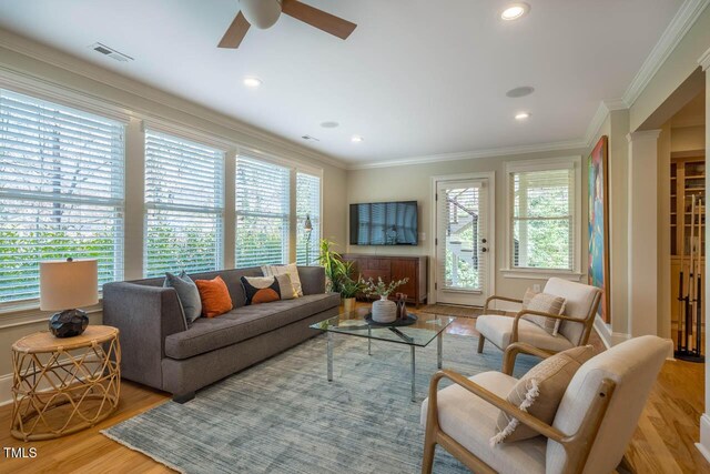 living room featuring a wealth of natural light, visible vents, crown molding, and light wood-style floors