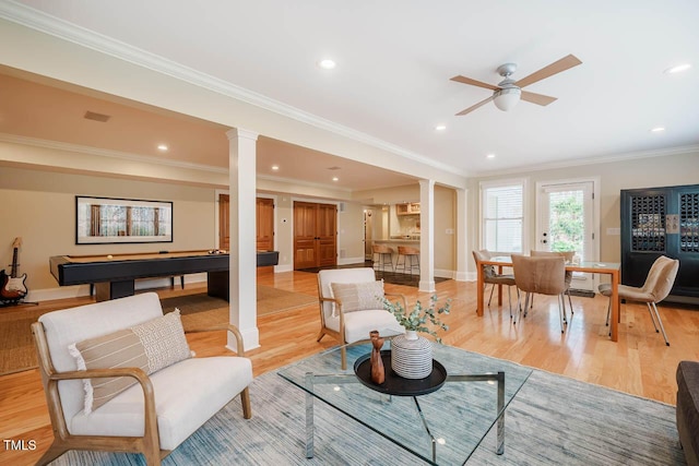 living area featuring recessed lighting, light wood-style flooring, crown molding, and decorative columns